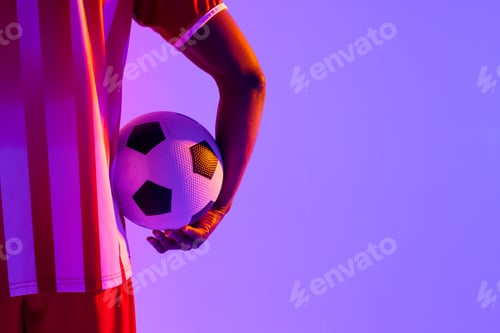 Preview: African american male soccer player with football over neon pink lighting