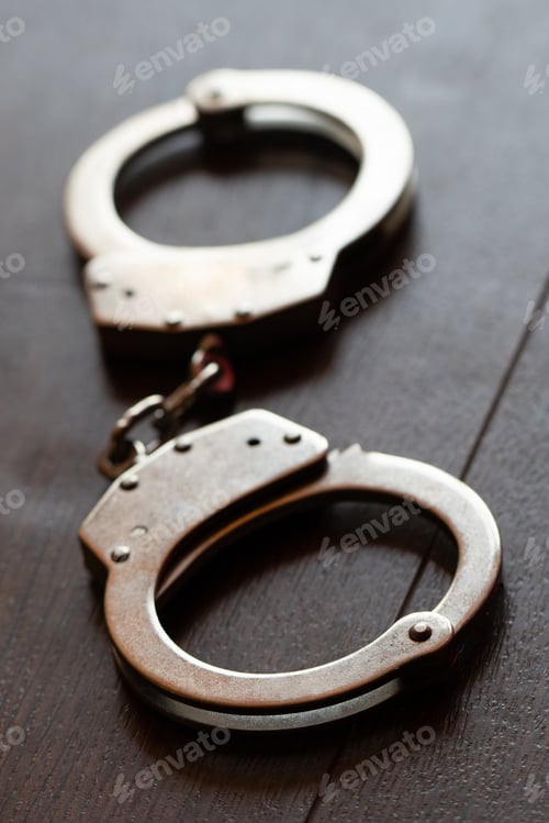 Preview: Vertical high angle shot of metal handcuffs on a wooden surface