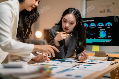 Preview: Businesswomen analyzing financial charts and graphs, working late in office