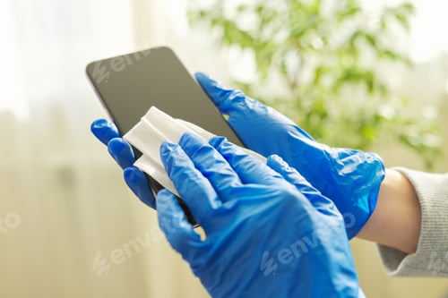 Preview: Close up of hands in rubber gloves disinfecting mobile phone