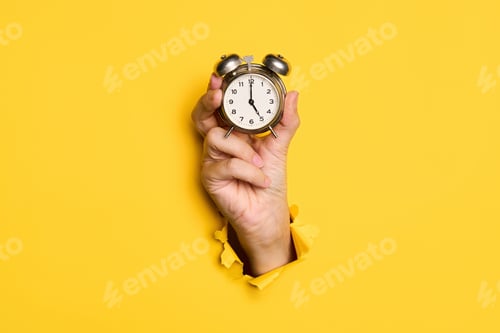 Preview: Vintage alarm clock in hand over yellow background