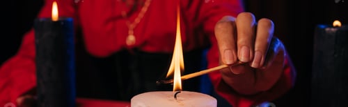 Preview: partial view of fortune teller lighting palo santo stick near burning candle isolated on black,