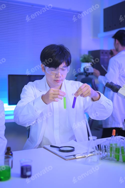 Preview: Scientist wearing safety goggles compares green and purple liquid samples in test tubes