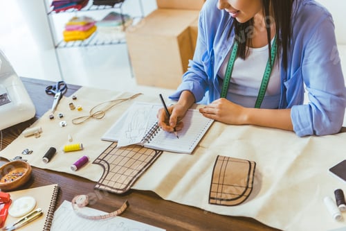 Preview: cropped image of seamstress writing down notes to notebook
