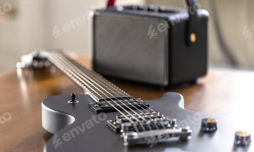 Preview: Black electric guitar and speaker on a wooden table.