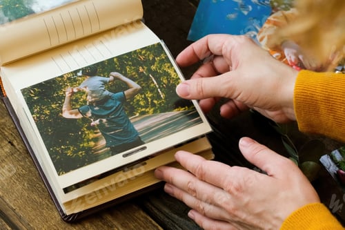 Preview: Photo printing concept. Female hands adding printed photo to picture album.