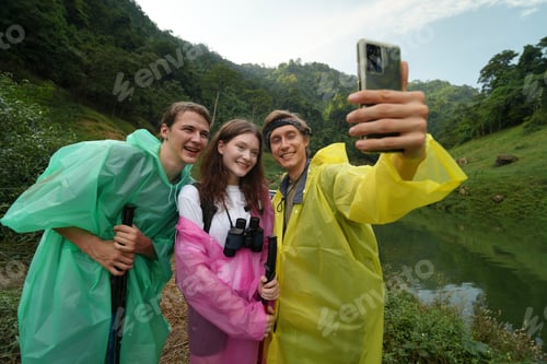 Preview: Friends taking a selfie while hiking in rain gear near a serene lake