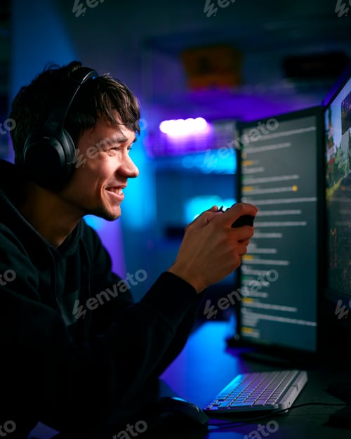 Preview: Low Key Lighting Shot Of Male Gamer In Front Of Computer Screens With Headphones And Controller