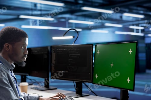 Preview: Engineer working on green screen PC in data center housing thousands of servers