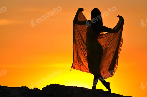 Vista previa: Silhouette of woman standing and holding pareo in raised hands at sunset