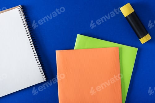 Preview: top view of blank notebook, glue stick and textbooks on blue background
