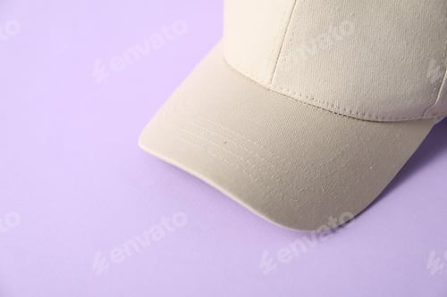 Preview: Beige baseball hat on violet background, closeup. Space for text