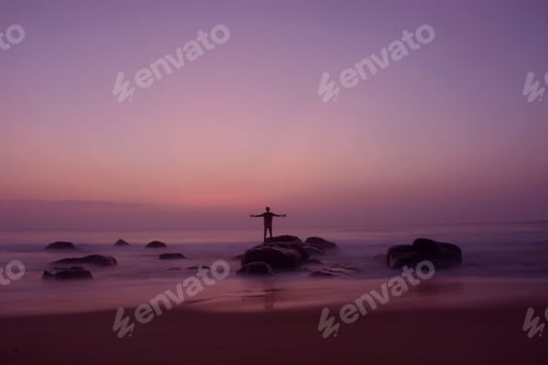 Preview: a man standing on top of a sandy beach at sunset