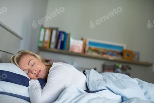 Preview: Adult woman sleeping with striped pillow and duvet under wooden shelf holding books and photograph