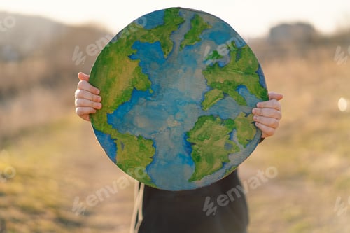 Preview: Little boy holding planet in hands against green spring background.