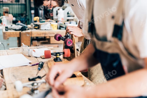 Preview: Young men in carpentry workshop looking down making skateboards
