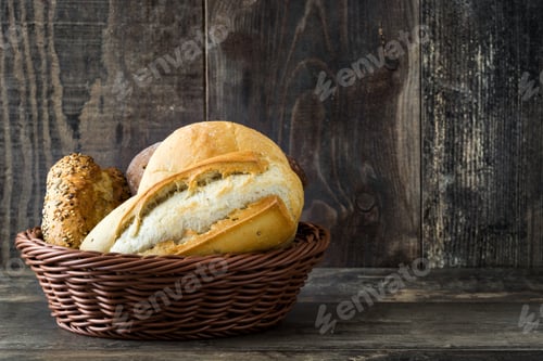 Preview: Basket overflowing with bread rolls and loaves on rustic wooden table
