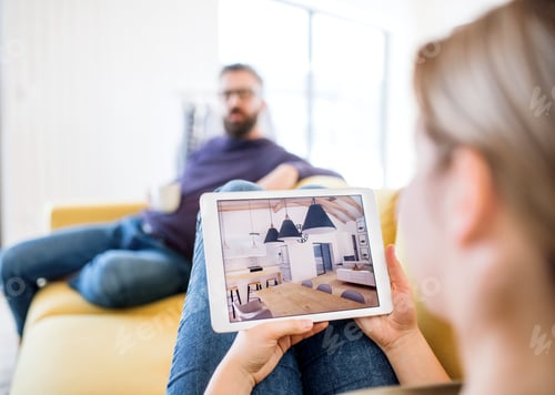 Preview: Young couple with tablet sitting on sofa, looking at interior design sketches.