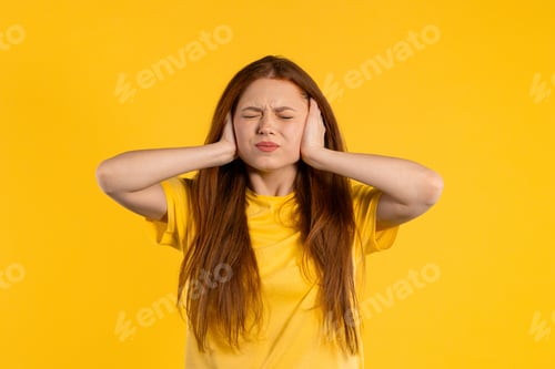 Preview: Irritated ginger woman with covered ears ignoring on yellow. Teenager banning annoying sounds
