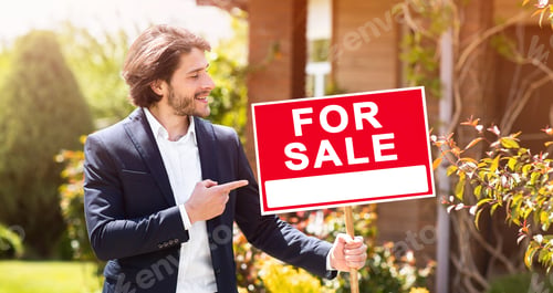 Preview: Confident real estate agent pointing at sign with words FOR SALE in front of residential building