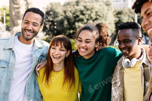 Preview: Happy multiracial young group of people hugging each other laughing at city