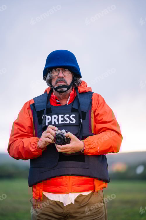 Preview: Reporter in bulletproof vest holding a camera.