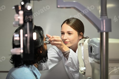 Preview: Female ophthalmologist checking eye vision of male patient with ophthalmic glasses in clinic.