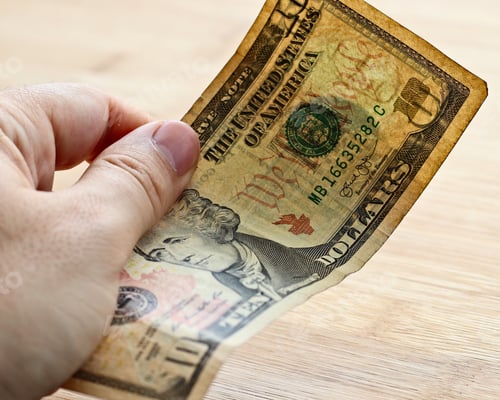 Preview: High angle shot of a person holding a dollar bill over a wooden surface