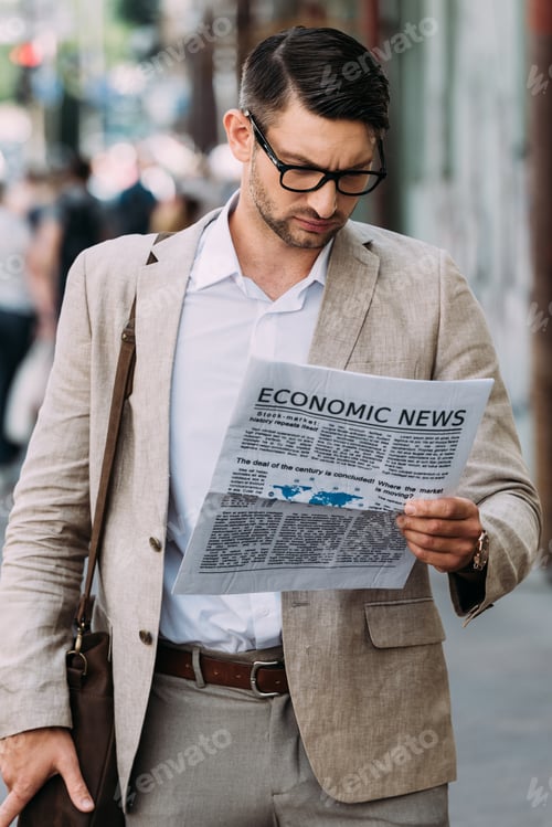 Preview: focused businessman in glasses reading newspaper on street