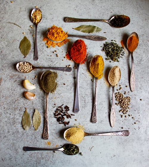 Preview: Top view of various spices in metal spoons with gray marble background.