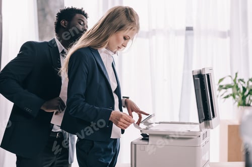 Preview: young businesspeople using copier together at office