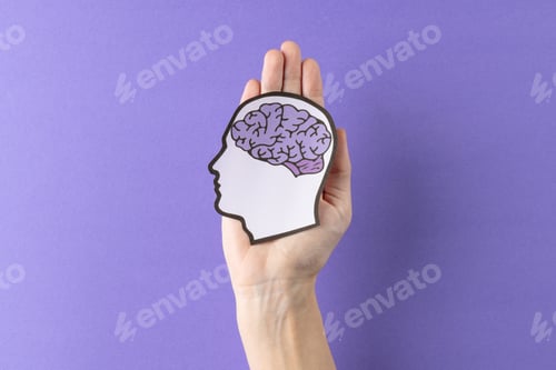 Preview: Composition of hands holding head silhouette with purple brain on purple background, with copy space