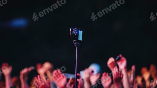 Preview: Closeup shot of a phone on a selfie stick and hands of a crowd during a concert