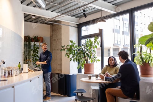 Preview: Colleagues chatting in modern office break room, man washing dishes