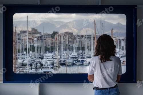 Preview: Woman looking through a window in a ferryboat with the port at the background, cruise, ship