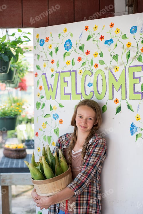 Preview: Summer on an organic farm. A girl holding a basket of fresh corn standing by the Welcome sign.