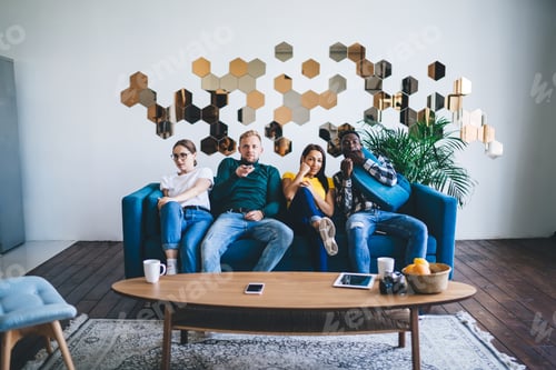Preview: Multiethnic friends watching TV while sitting on sofa