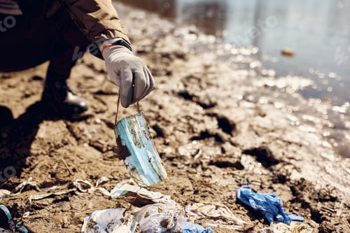 Preview: Close-up of man picking up dirty face mask while cleaning garbage on the beach.