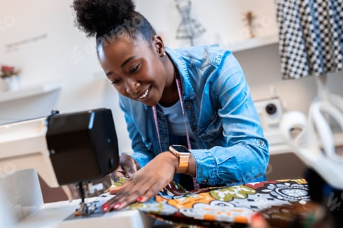 Preview: Female fashion tailor with sewing machine working on dress design in her workshop.