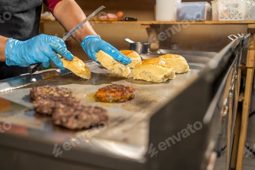 Preview: Cook preparing bread for delicious burgers on hot grill in restaurant kitchen
