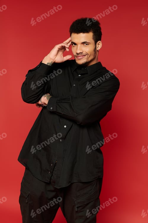 Preview: Handsome young man poses confidently against a vibrant red background in stylish outfit