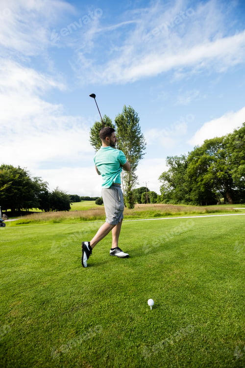 Preview: Male golfer striking ball on golf tee beside white tee marker wearing teal polo shirt