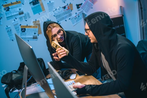 Preview: happy couple of hackers with stack of cash at workplace