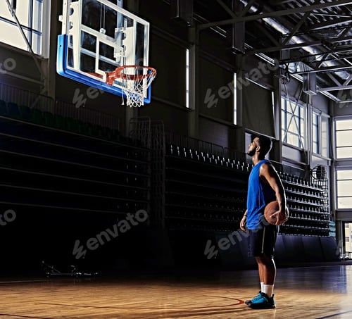 Preview: Basketball player holds a ball over the hoop in a game hall.