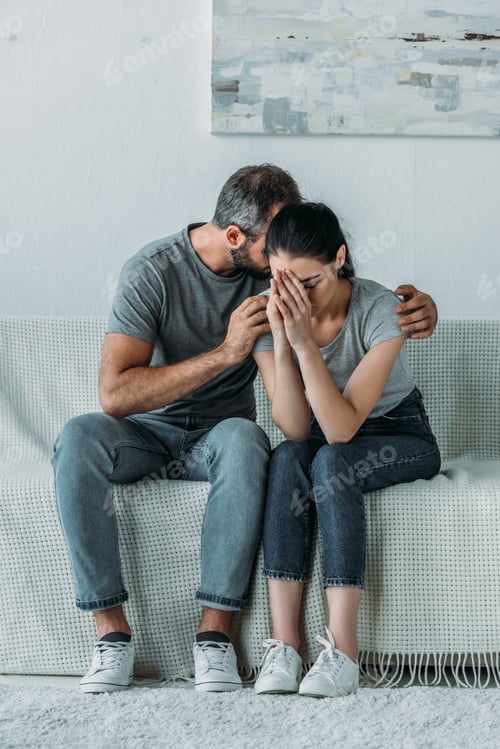 Preview: upset young man supporting depressed girlfriend while sitting together on couch