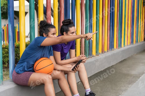Preview: Female basketball players pointing, resting beside colorful fence