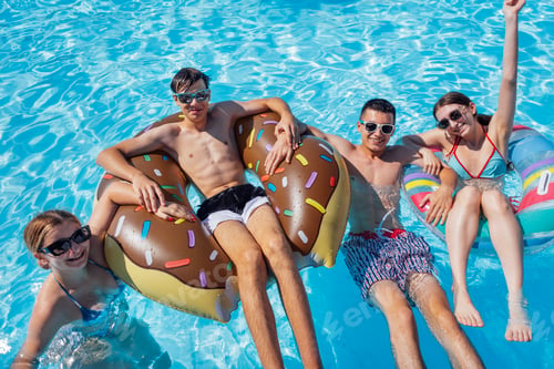 Preview: Smiling teenagers in swimsuits and sunglasses swim in the pool.