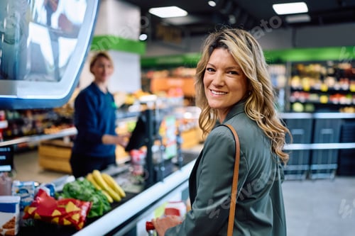 Preview: Happy woman paying for groceries in supermarket at looking at camera.