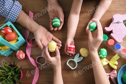 Preview: Father, mother and their child holding painted Easter eggs on wooden background, top view