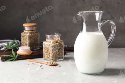 Preview: Composition with pitcher of hemp milk on marble table against grey background. Space for text